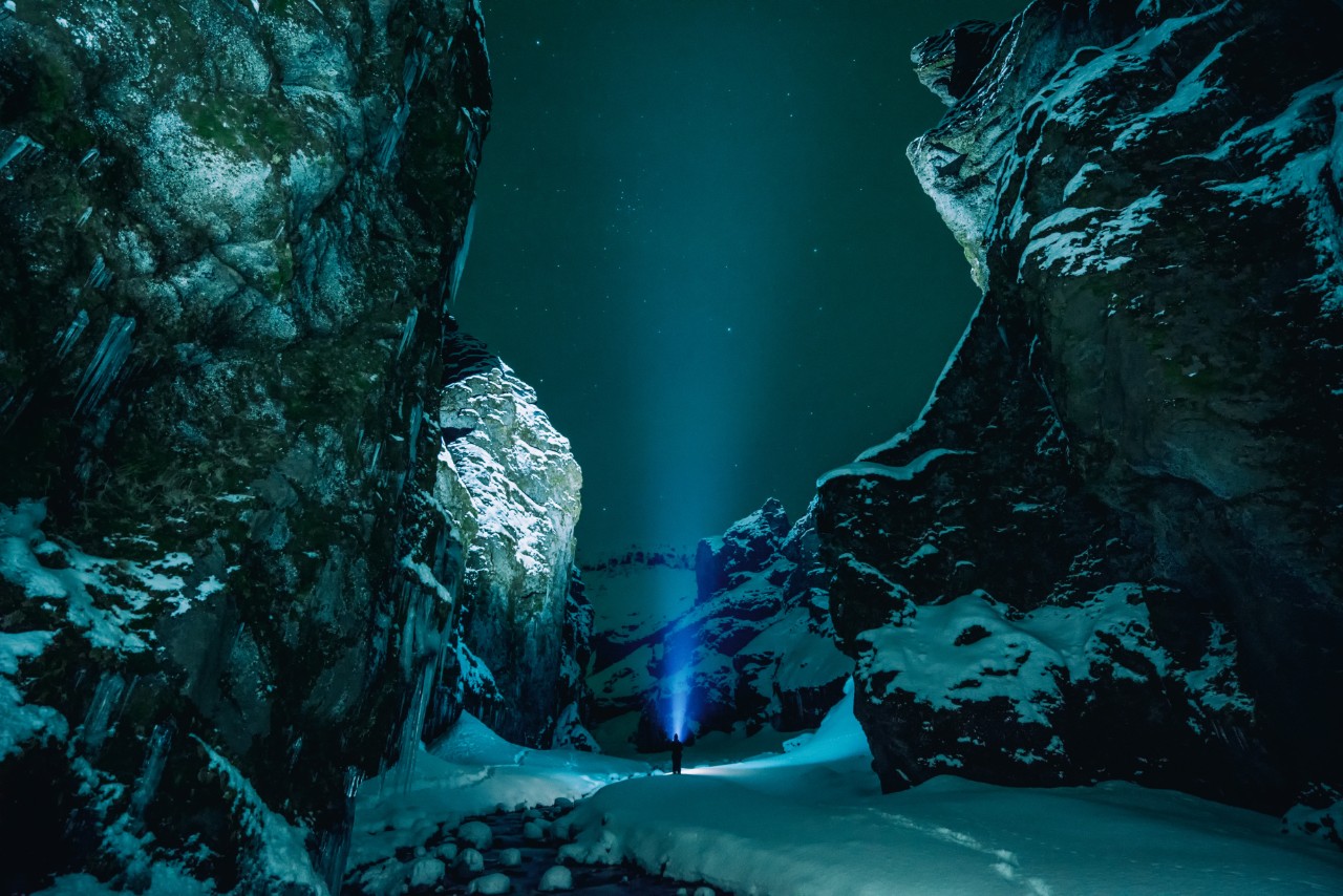 cover page photo of man standing in a wintry, snowy landscape aiming his flashlight/spotlight upwards to the night sky.